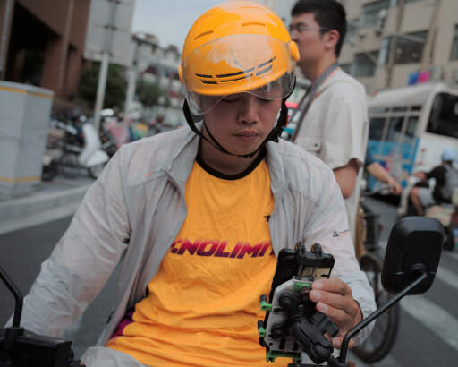 A picture taken while a Chinese delivery driver waits for the signal light; I'm unsure if he is scrolling for pleasure or just planning his next delivery. 